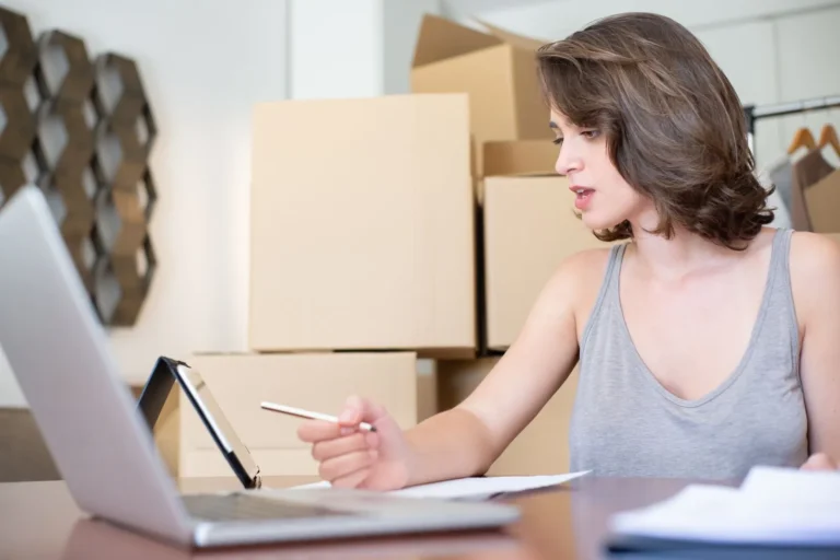 Online seller reviewing orders on a laptop among parcels